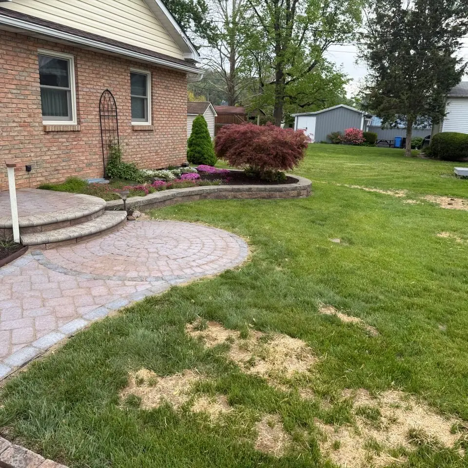 Paver walkway curving through a front lawn with landscaped beds in front of a brick home