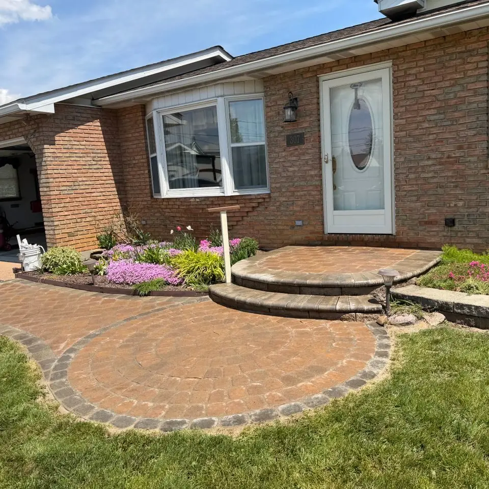 Brick paver patio and steps in front of a brick home with flowering beds